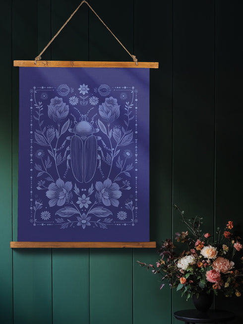 A symmetrical wall tapestry in monochromatic navy blue featuring a detailed scarab beetle surrounded by flowers and botanical elements, mounted on a wooden dowel with natural twine.